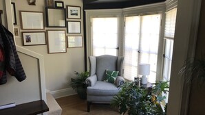 Ein gemütliches Wohnzimmer mit einem grauen Sessel, einer Topfpflanze und einer Treppe mit Garderobe.