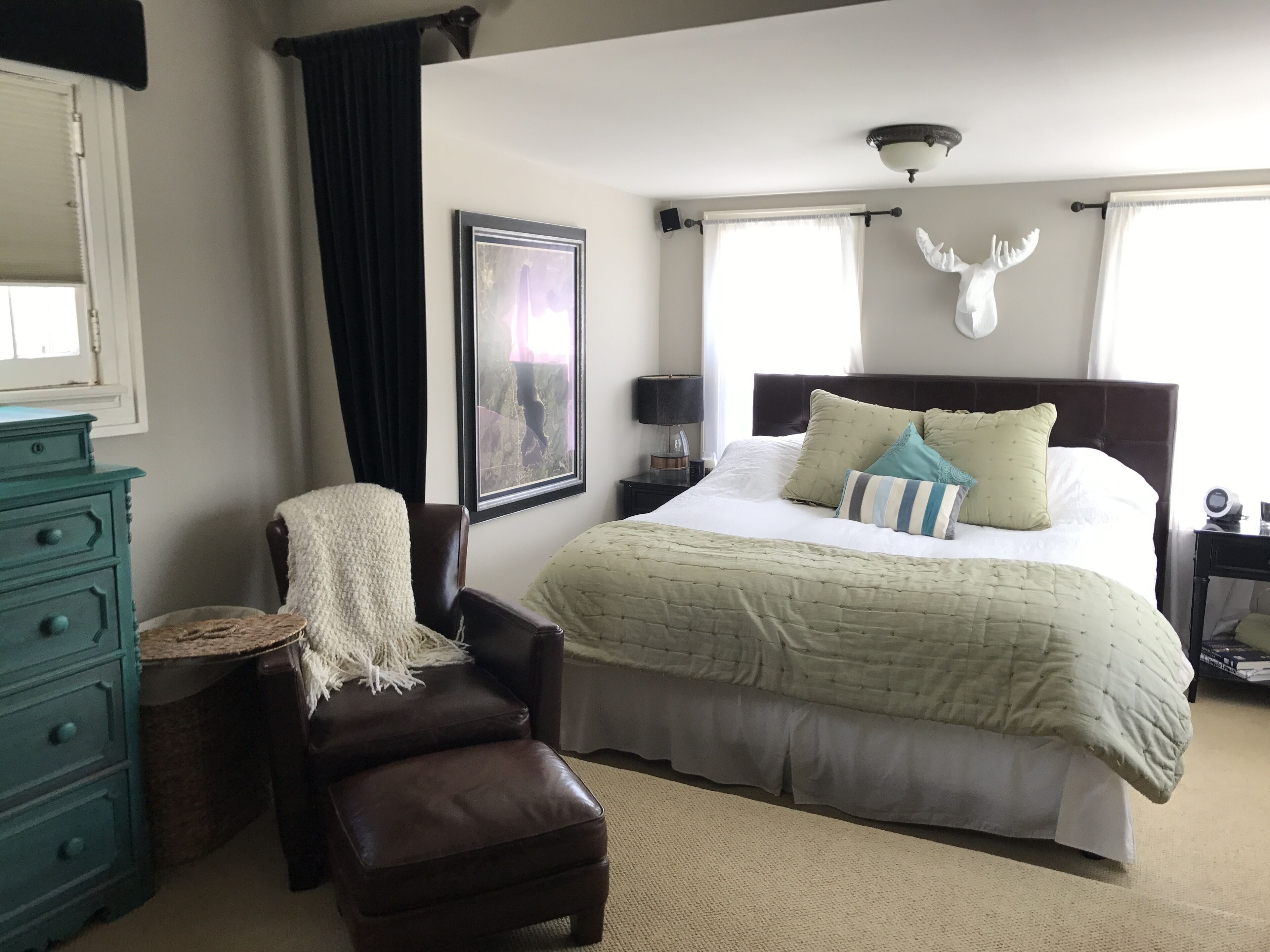 A bedroom with a bed, a chair, a dresser, a framed picture, and a wall-mounted light fixture.