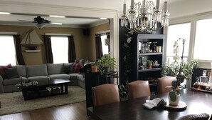 Ein Wohnzimmer mit einem dunklen Holzesstisch, Ledersesseln, einem grauen Sofa und einem schwarzen Bücherregal.