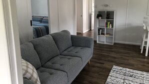 Una sala moderna con un sofá gris, una estantería blanca y una alfombra estampada.