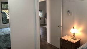 Un pasillo con una cama, una lámpara y una puerta que da a otra habitación.