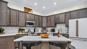 A modern kitchen with dark wood cabinets, a white countertop, a central island with a wooden bowl, and stainless steel appliances. - Historic Levy Penthouse Downtown Louisville (Louisville)