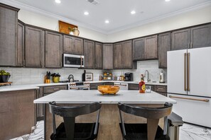 A modern kitchen with dark wood cabinets, a white countertop, a central island with a wooden bowl, and stainless steel appliances. - Historic Levy Penthouse Downtown Louisville (Louisville)