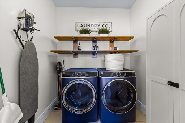 A laundry area with two front-loading washing machines, a drying rack, and a shelf with plants and a sign that reads 'LAUNDRY CO.'