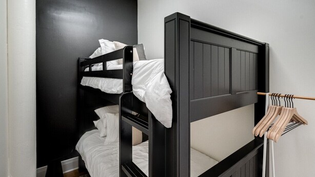 A bunk bed with white bedding, a wooden wardrobe, and a clothing rack. - Historic Levy Penthouse Downtown Louisville (Louisville)