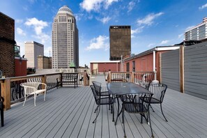 An outdoor deck with a table and chairs, overlooking a cityscape with tall buildings.