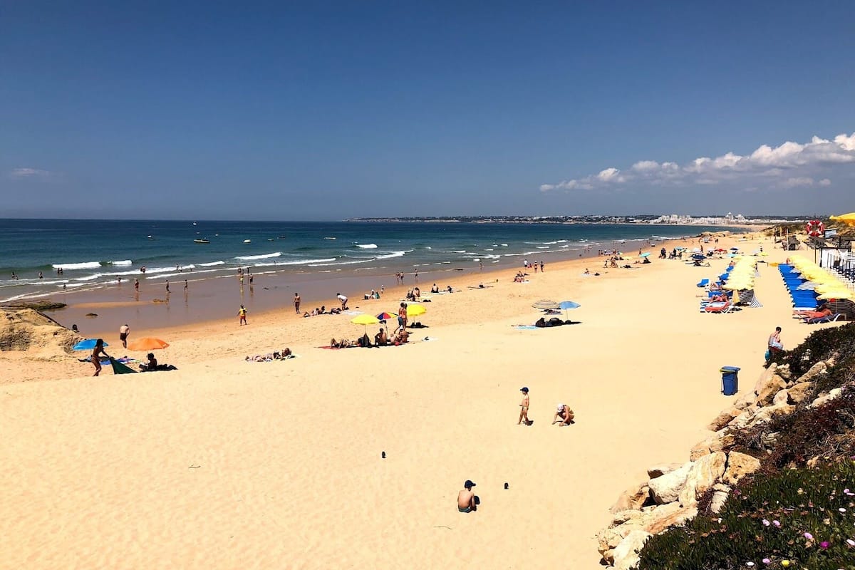 Une vaste plage de sable, parsemée de parasols et fréquentée par de nombreuses personnes.