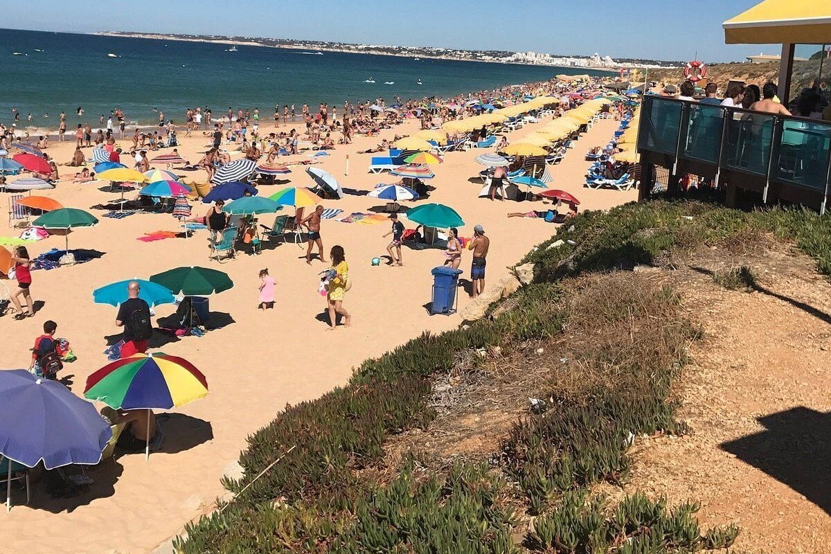 Une plage bondée, avec de nombreux parasols colorés et des gens qui profitent du soleil.