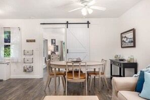 Un coin repas avec une table ronde et des chaises, un ventilateur de plafond et une vue sur la cuisine.