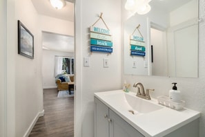 Une salle de bain moderne avec un lavabo blanc, un grand miroir et un panneau d’accueil.
