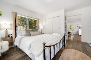 A bedroom with a large bed, a window, a bedside table with a lamp, and a wardrobe.