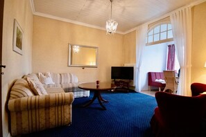 A living room with a sofa, a TV, a coffee table, and a red chair. - Villa Wilhelma Apartment 6 - Villa Wilhelma Strandallee 146 (Timmendorfer Strand)