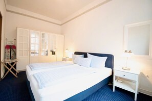 A hotel room with a large bed, a wardrobe, a bedside table with a lamp, and a mirror on the wall.