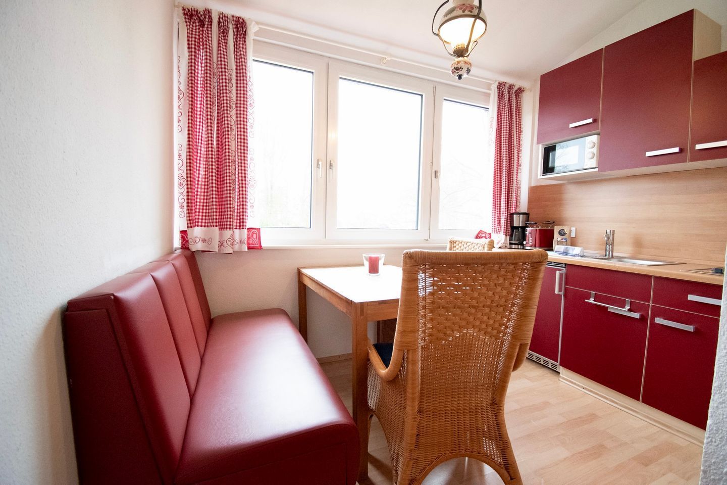 Una cocina pequeña con armarios rojos, una mesa de madera y una silla de mimbre.