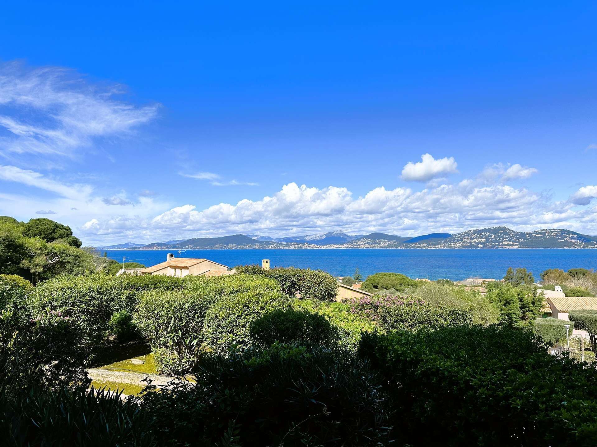 A coastal landscape with a clear view of the sea, a mountain range in the distance, and lush greenery in the foreground.