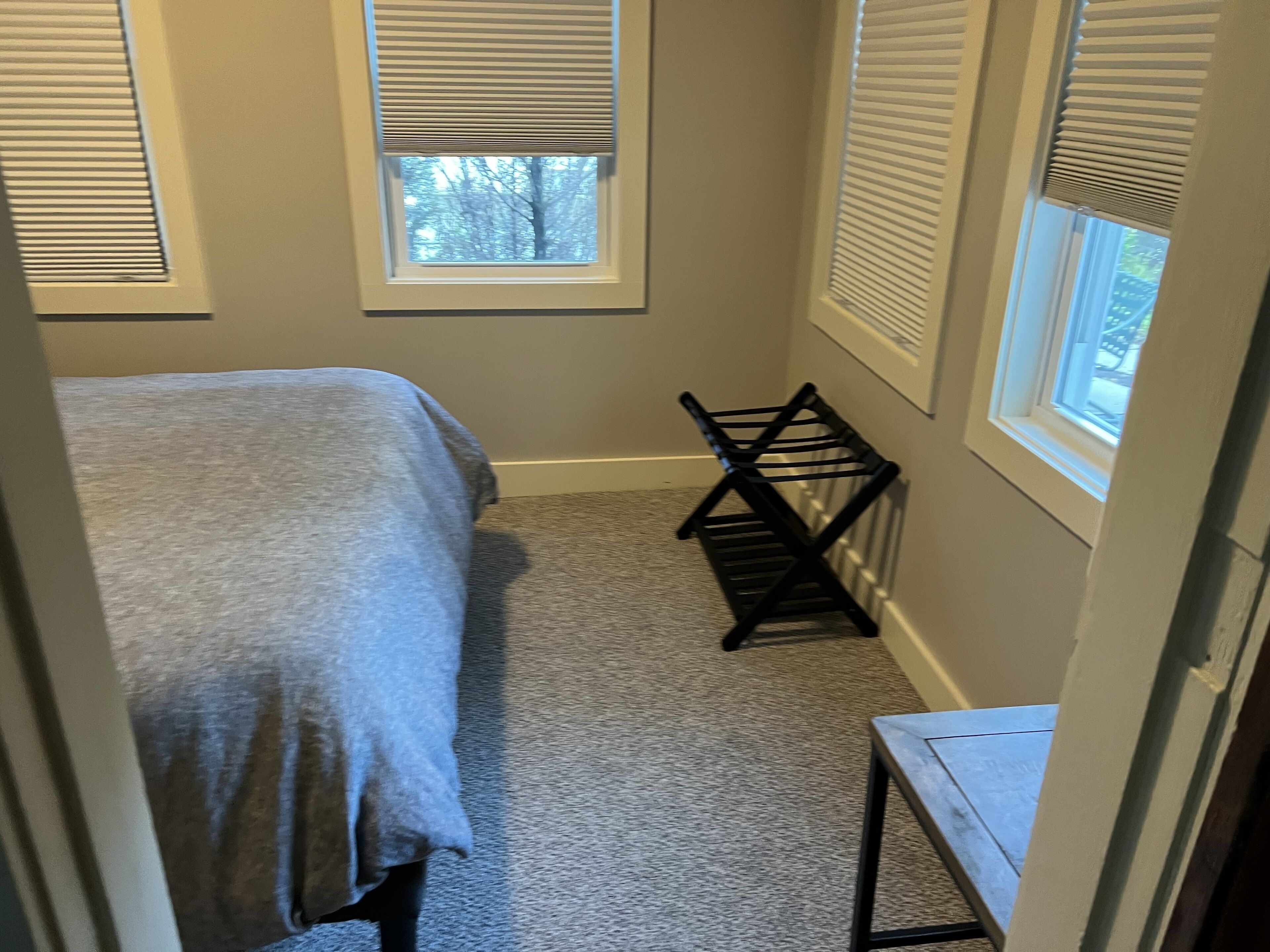 Un dormitorio con cama, una mesita pequeña y una ventana con persianas.