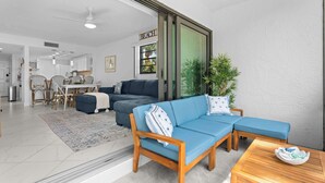 A modern living room with a sectional sofa, wooden coffee table, and a dining area with wicker chairs. - First Floor Corner Condo at Park Shore Resort 149 (Naples)
