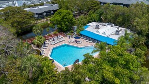 An aerial view of a hotel with a large swimming pool surrounded by lush greenery and a red bridge. - First Floor Corner Condo at Park Shore Resort 149 (Naples)