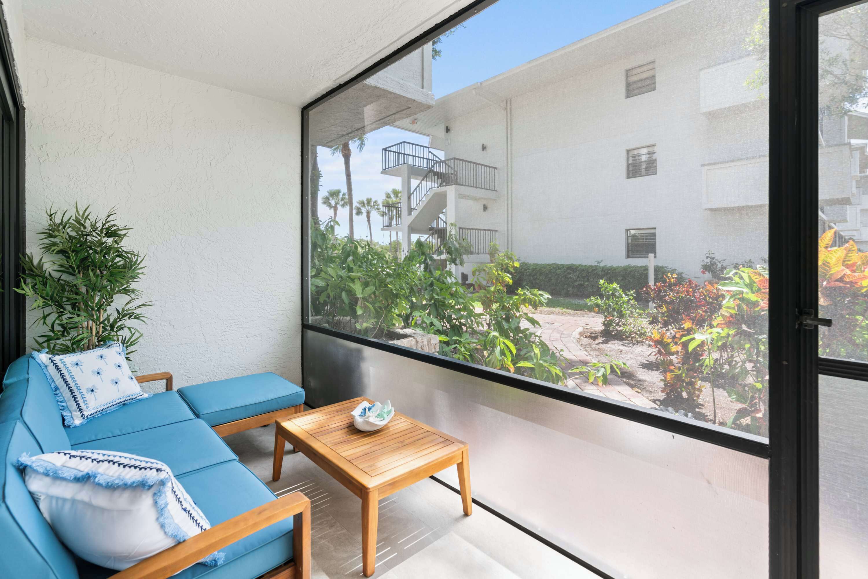 Un balcon avec un canapé bleu, une table en bois et une vue sur un immeuble doté de balcons et de plantes.