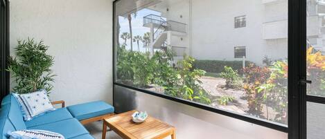 Un balcon avec un canapé bleu, une table en bois et une vue sur un immeuble doté de balcons et de plantes.