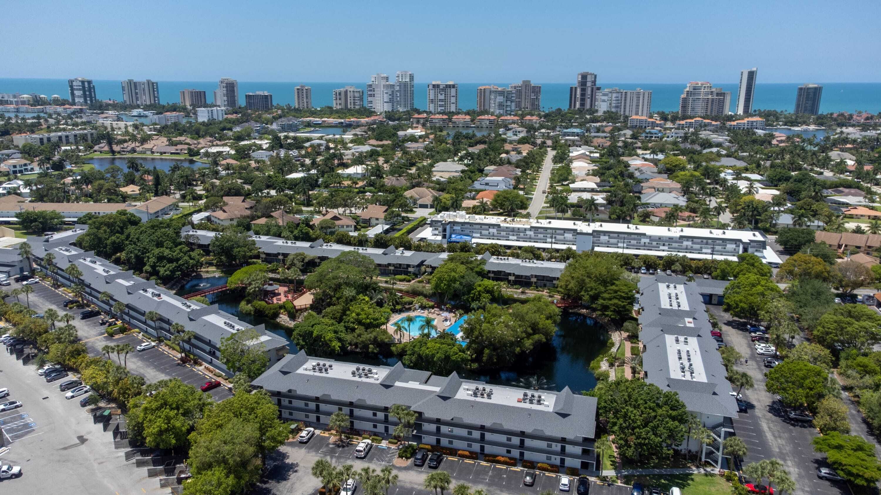 A large hotel complex with multiple buildings, a central pool area, and a view of the ocean.