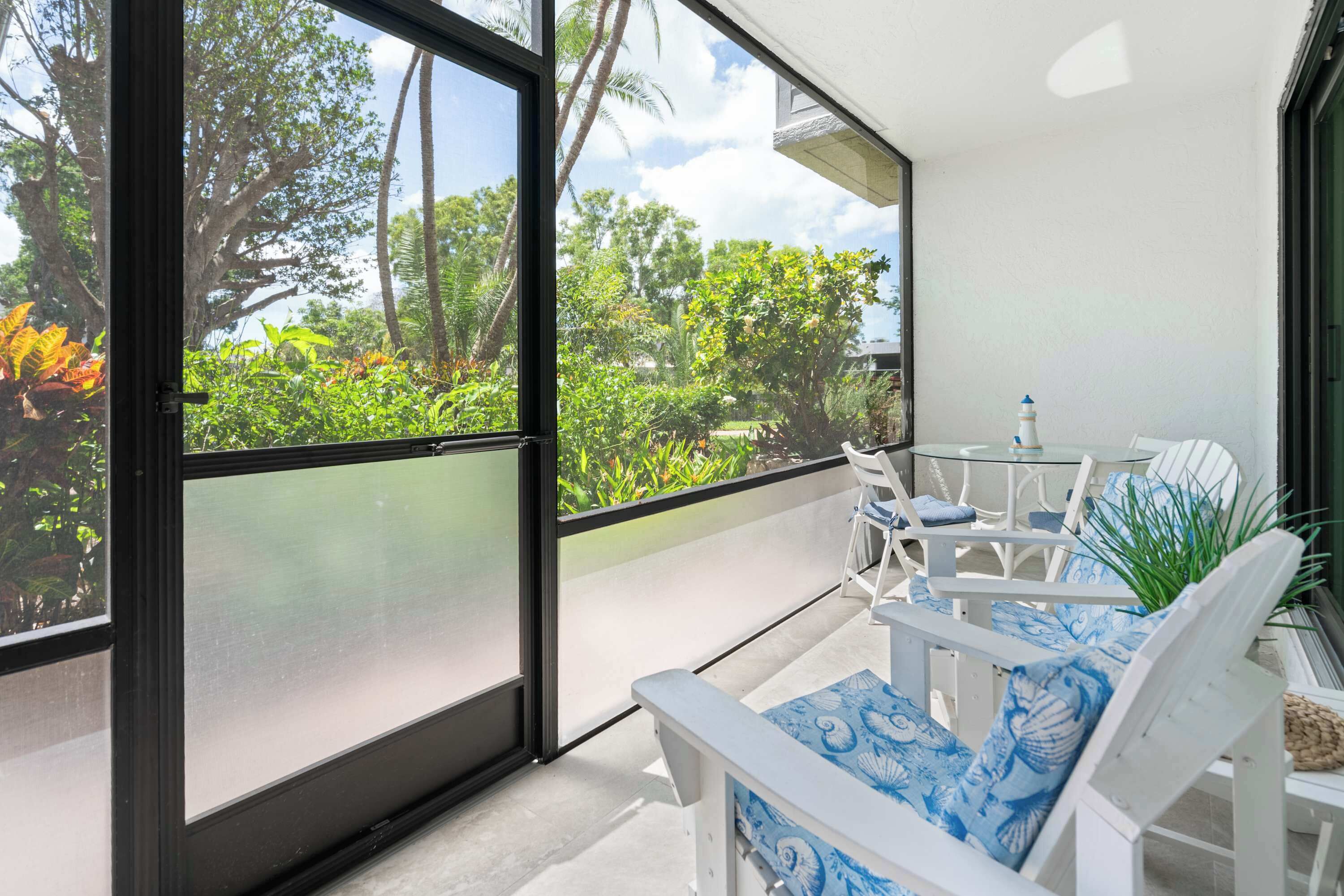 Un balcon doté d’une porte vitrée, de mobilier d’extérieur blanc et offrant une vue sur une végétation tropicale.