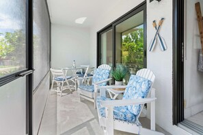 A balcony with white chairs and a table, a potted plant, and a view of trees.