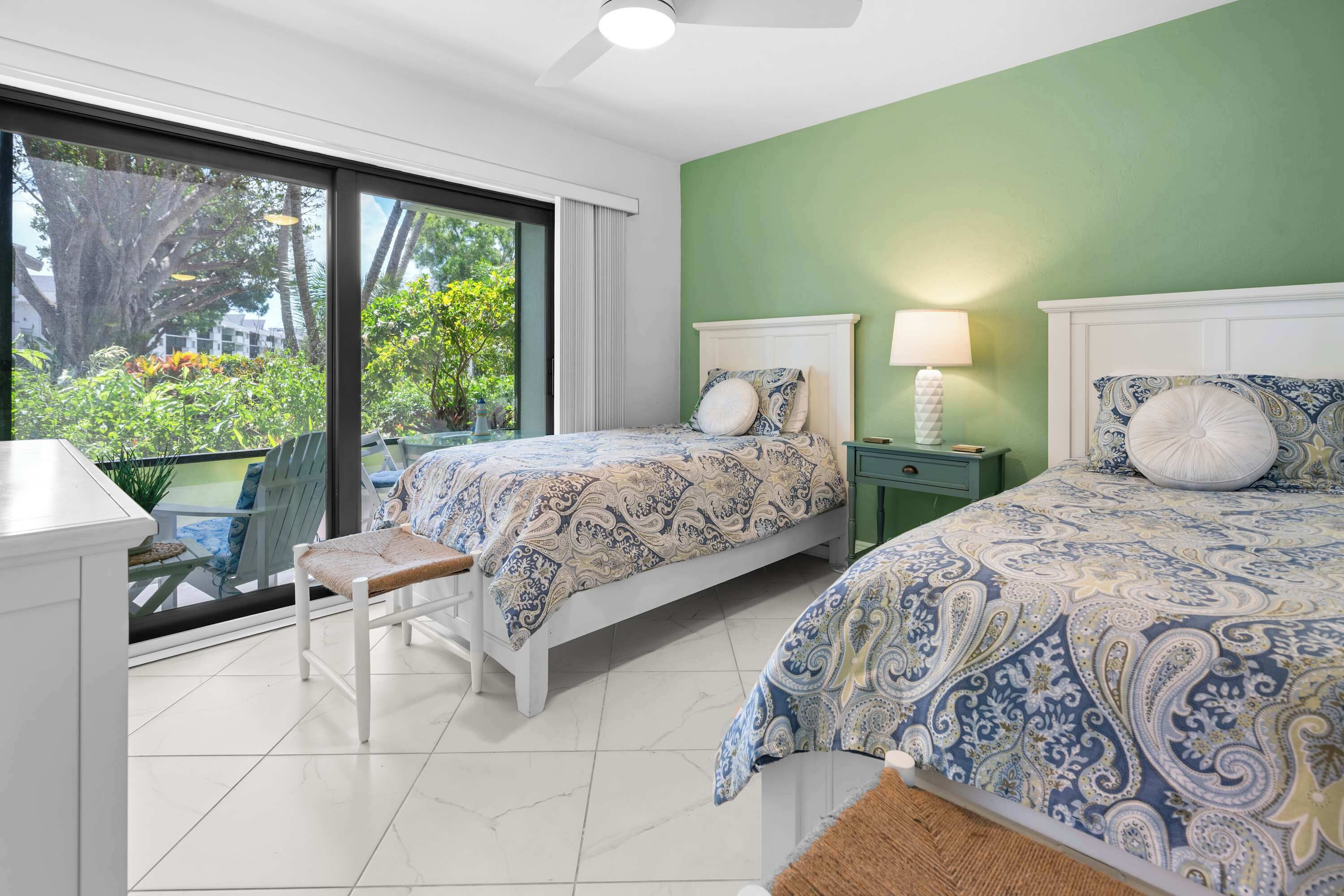 Une chambre avec deux lits, une fenêtre donnant sur un paysage verdoyant et une petite table avec une chaise.