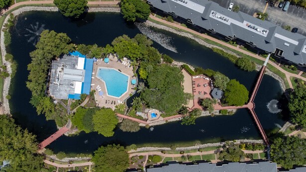 An aerial view of a resort with a large swimming pool, a separate pool area, and a bridge connecting different parts of the property. - First Floor Corner Condo at Park Shore Resort 149 (Naples)