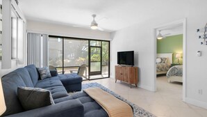 A modern living room with a large sofa, a television, and a sliding glass door leading to a balcony. - First Floor Corner Condo at Park Shore Resort 149 (Naples)