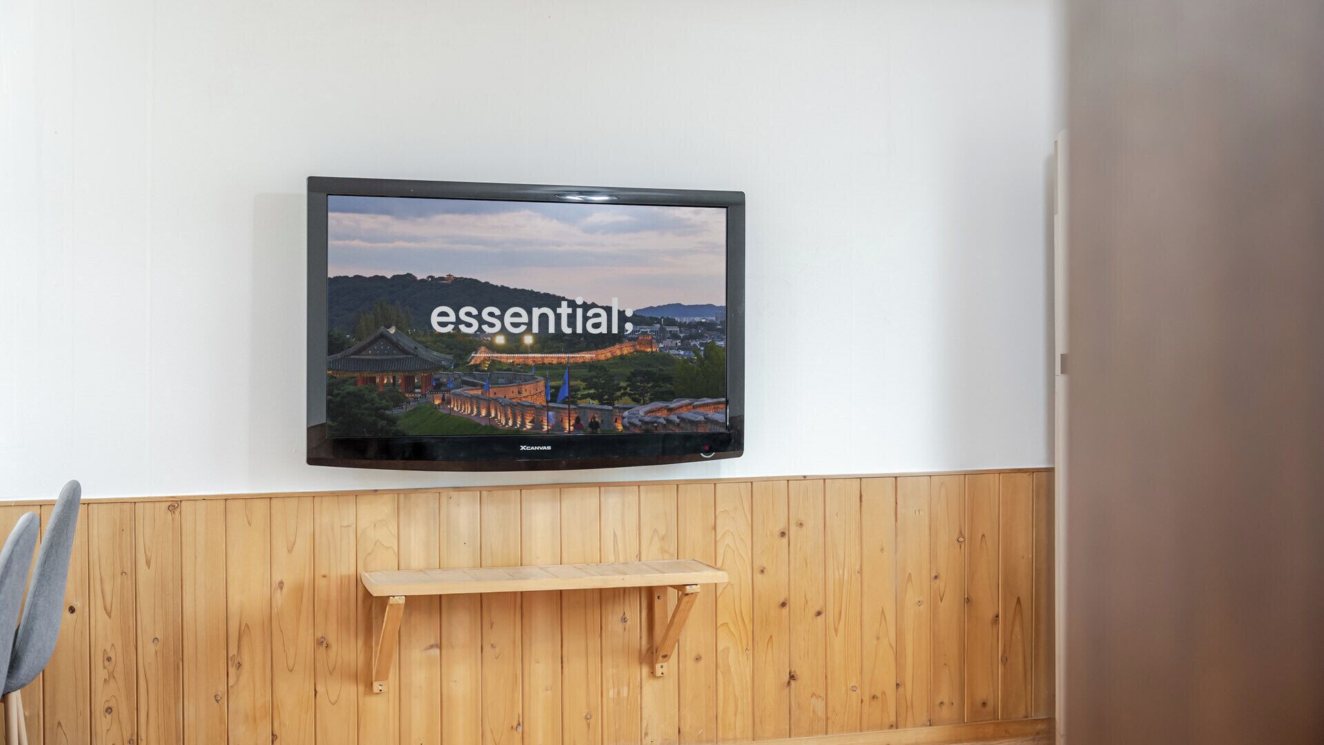 Ein Flachbildfernseher an einer weißen Wand, unterhalb davon eine Holzvertäfelung.