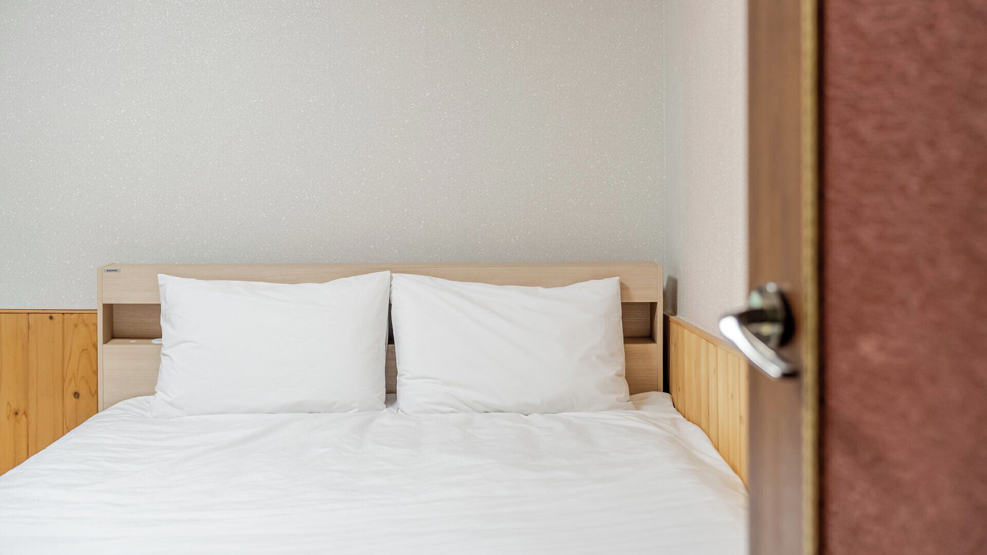 A bed with a wooden headboard and white bedding in a room with a plain wall.