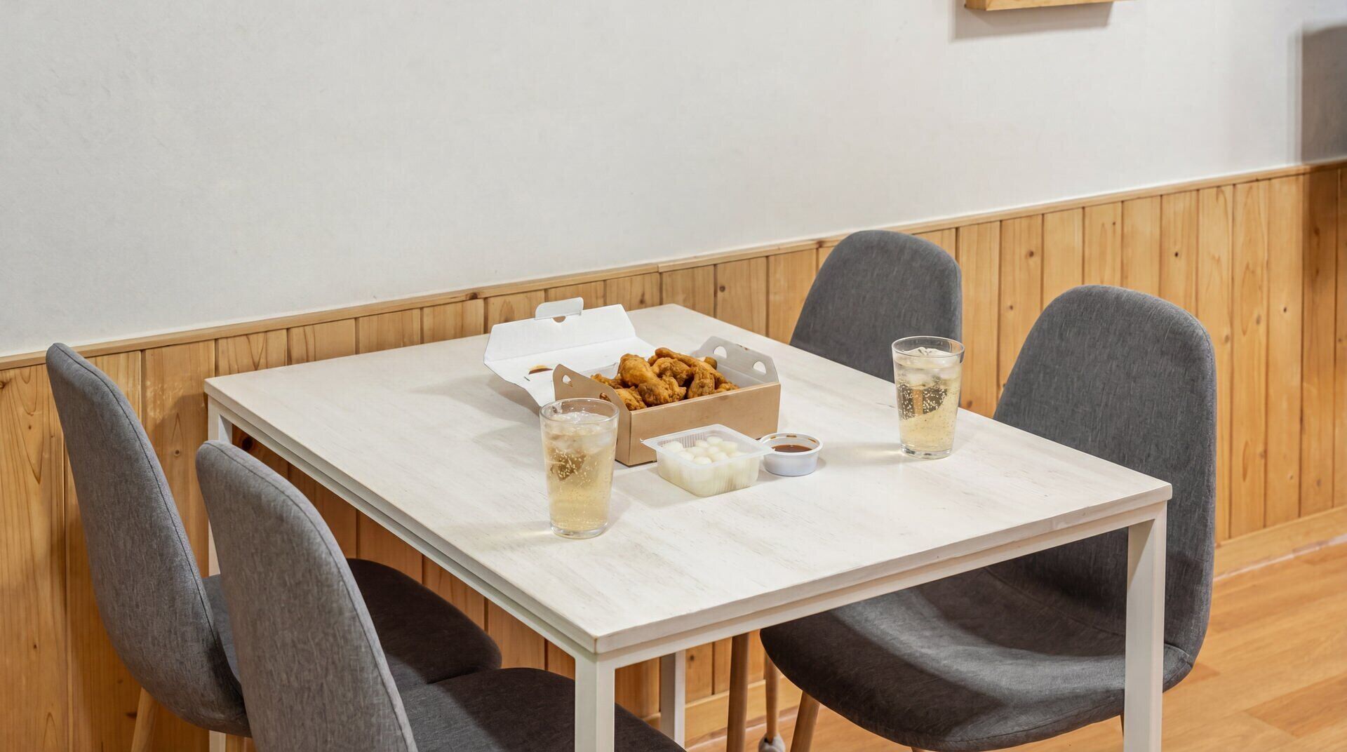 A dining table with a box of fried chicken, two glasses of iced tea, and condiments.