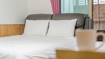 Una cama con ropa de cama blanca, cabecera de madera y ventana con vista a un edificio.