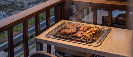 A barbecue grill with steaks, sausages, and vegetables on a balcony.
