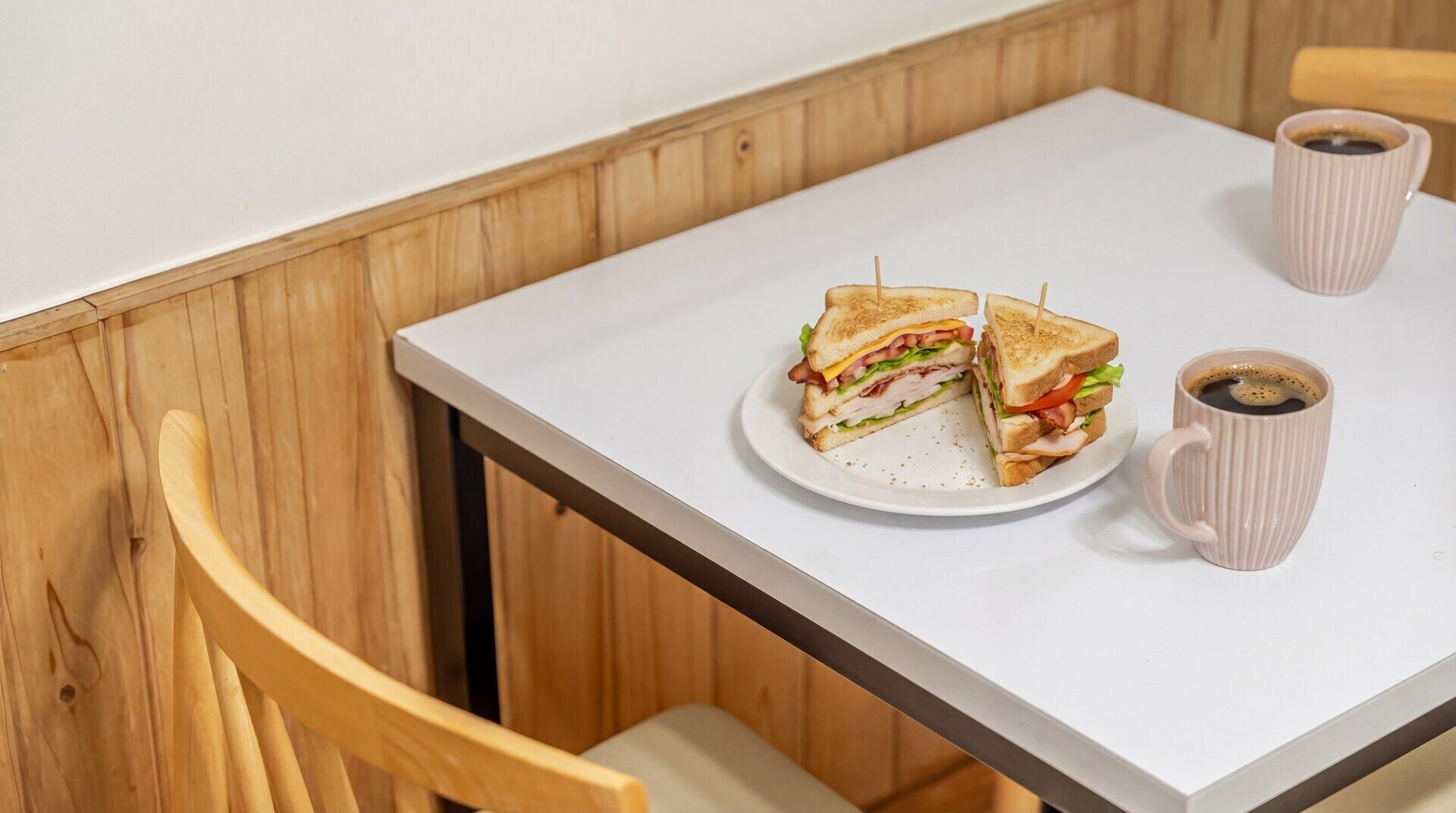 Un sándwich en un plato con una taza de café sobre una mesa.