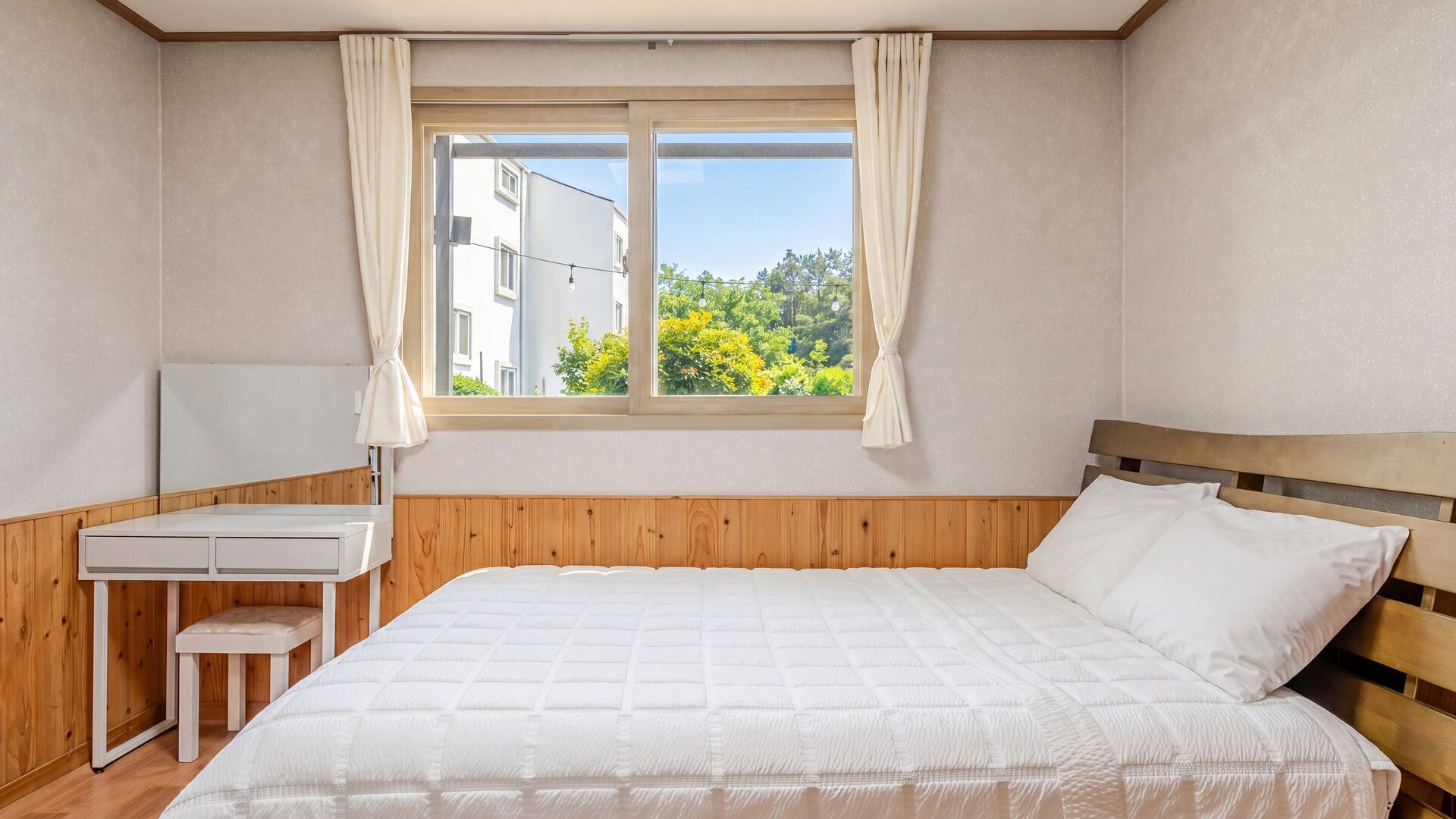 A bedroom with a bed, a desk, and a window with curtains.