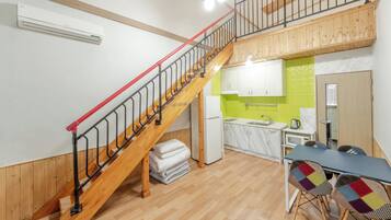 A multi-level apartment with a wooden staircase, a kitchen with a green backsplash, and a dining area with a table and chairs.