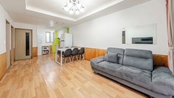 Una sala moderna con un sofá gris, piso de madera, un comedor con sillas, una cocina con microondas y un espejo grande en la pared.