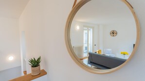 A modern living room with a round mirror, a wooden shelf with a plant, a grey sofa, and a small table with yellow flowers. - Ponente Balcony in Gravedona (Gravedona)