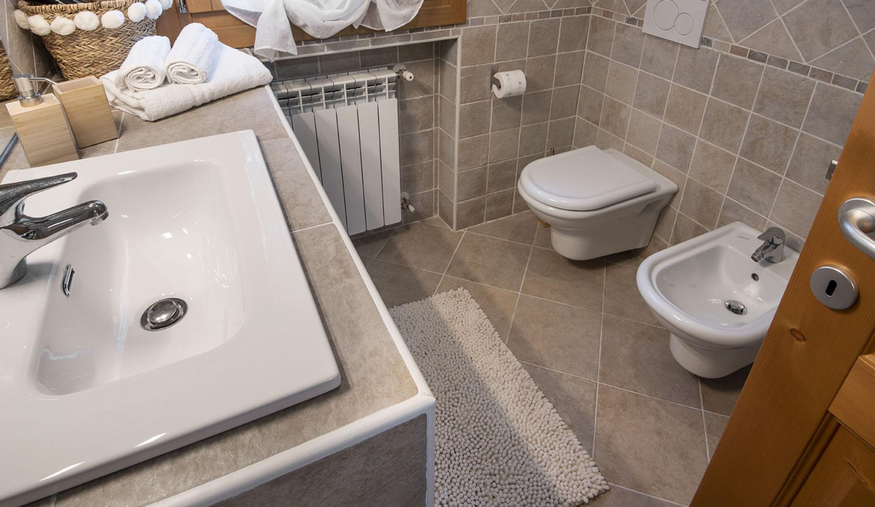 A modern bathroom with a large sink, toilet, bidet, and a towel rack.