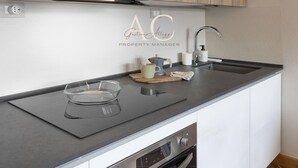 Una cocina moderna con encimera negra, horno de acero inoxidable y un lavabo con grifo. Hay un logotipo en la pared sobre el lavabo.