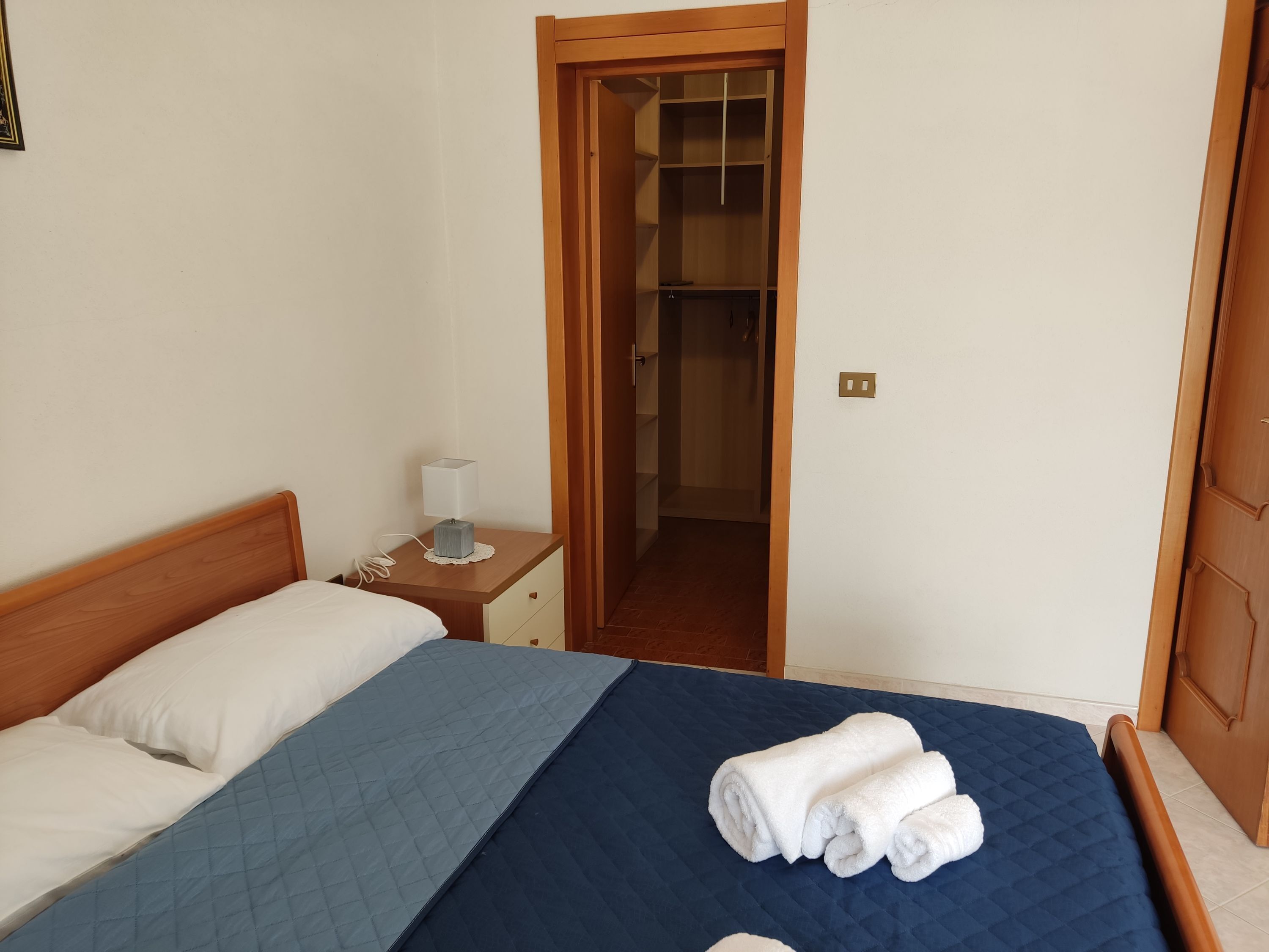 A bedroom with a bed, a nightstand, a lamp, and a door leading to a closet.