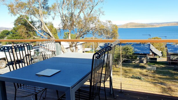 A deck with a table and chairs overlooking a body of water and hills.
