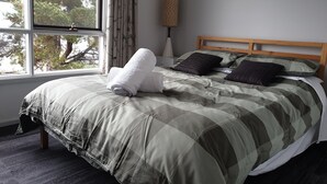 A neatly made bed with a checkered bedspread, two pillows, and a rolled white towel.