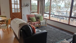 A cozy room with a sofa, armchair, and a dining table. There is a large window with a view of the outside.