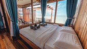 A wooden cabin room with a bed, curtains, and a view of the sea. - Larapan Water Village Semporna  (Larapan Island)