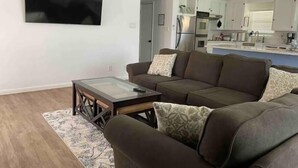 A modern living room with a brown sofa, a glass coffee table, and a flat-screen TV mounted on the wall. - Awesome Pool House in the Kern River Valley (Wofford Heights)