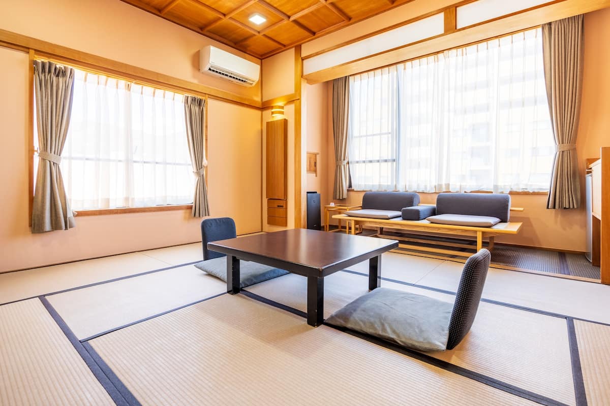 A traditional Japanese room with tatami flooring, a low table, cushions, and a sofa.