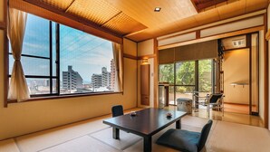 A traditional Japanese-style room with tatami flooring, a low table, and a view of the city through large windows. - Oyado Uoki (Yugawara)